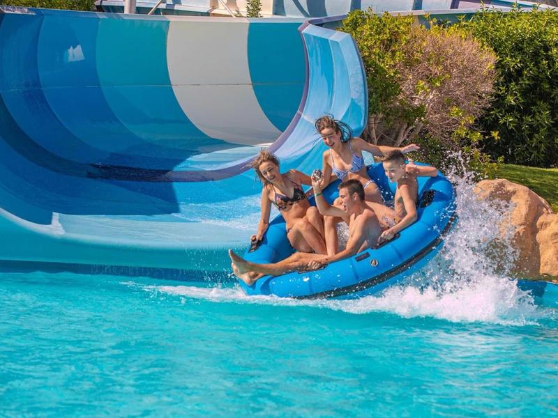 Sechs Personen auf blauer Reifenrutsche fahren in klarem Wasser mit Wasserfall.