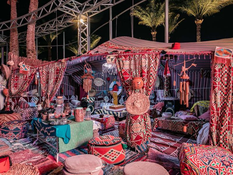 Bunter Marktstand mit traditionellen Teppichen, Textilien und Kissen unter Palmen bei Nacht.