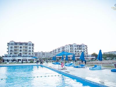 Gran piscina al aire libre con sombrillas azules y edificio de hotel de varios pisos al fondo.