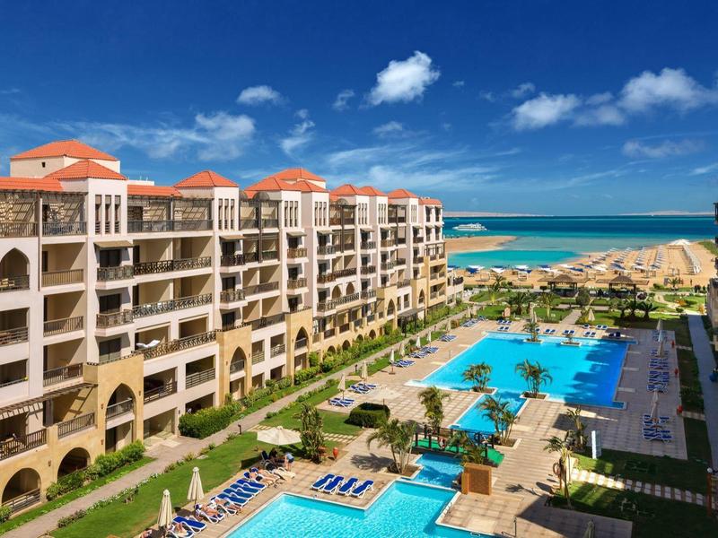 View of a large resort with pools, umbrellas, and sea in the background