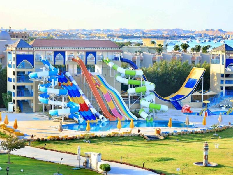 Colorful water slides in a water park in front of a hotel with mountains in the background.