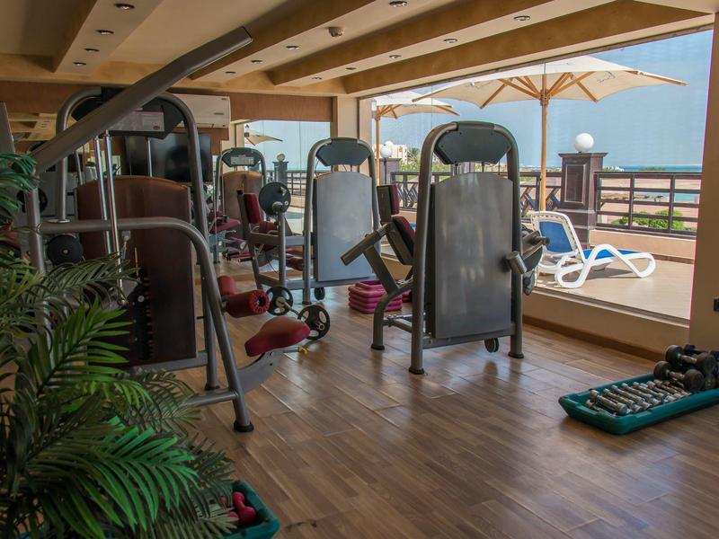 Covered gym area with equipment and view of loungers and mountains in the background.