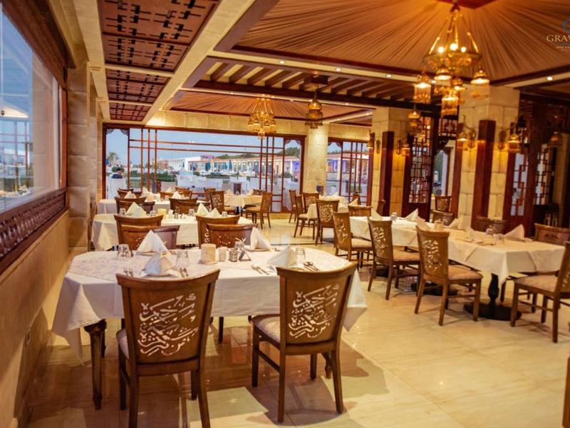 Elegant hotel restaurant with decorated ceiling, wooden furniture, and white tablecloths.