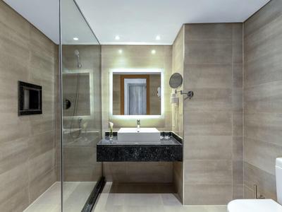 Moderne hotelbadkamer met glazen douche, zwart wastafelblad en beige betegelde muren.