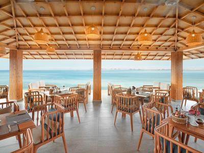 Openlucht restaurant met houten tafels en stoelen gericht op de oceaan onder een rieten dak.