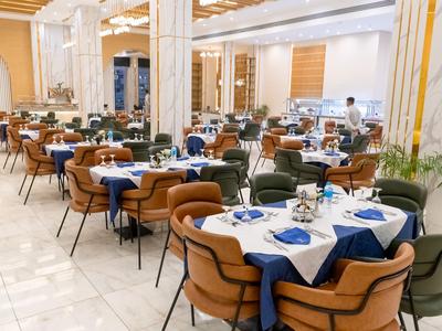 Restaurante elegante con mesas blancas, sillas marrones y servilletas azules en una habitación luminosa.