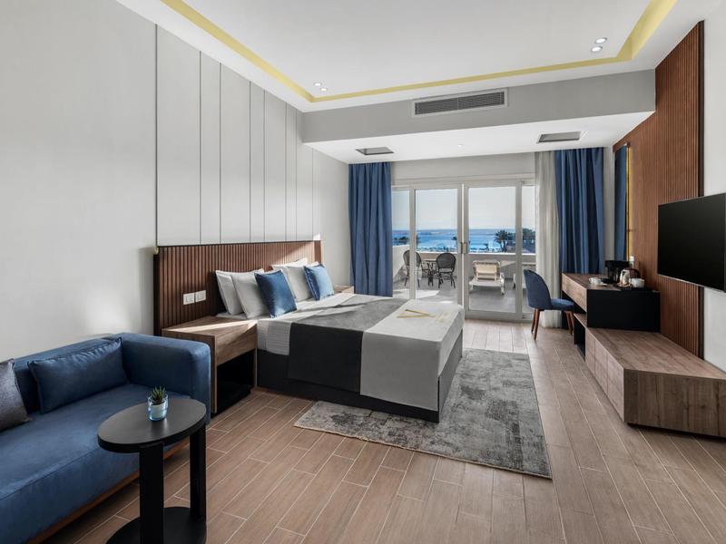 Hotelkamer met kingsize bed, blauwe bank, balkon, tv en moderne meubels.