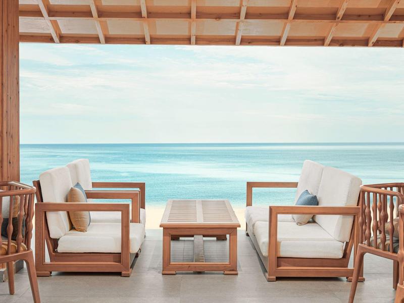 Buitenzitje onder een houten dak met uitzicht op de oceaan en comfortabele witte kussensstoelen.