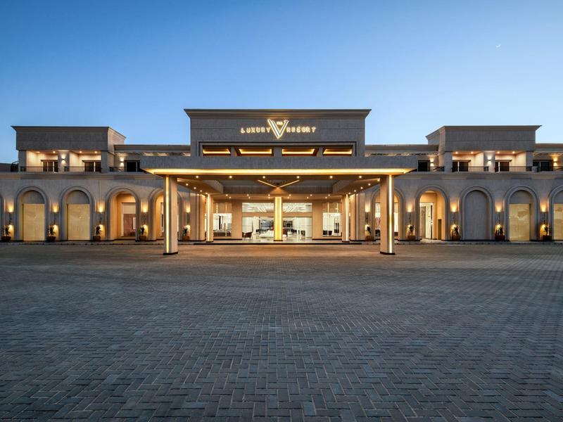 Luxe hotelentree met warme verlichting en ruime oprit bij schemering.