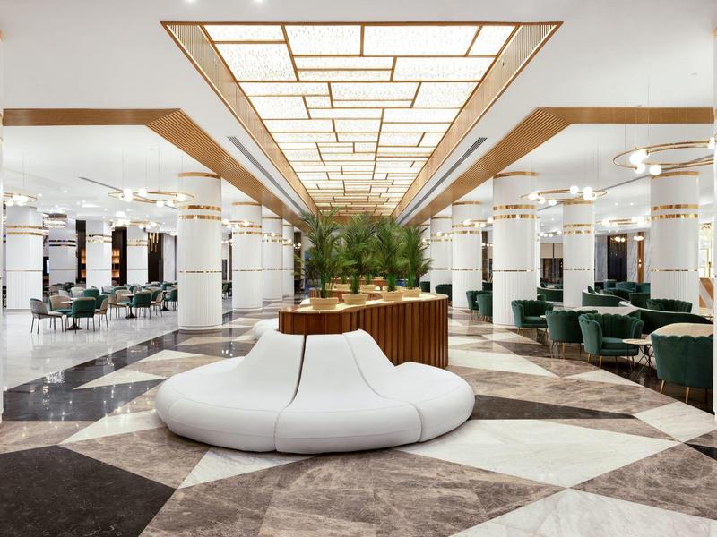 Luxueuze hotelhal met moderne witte zitjes, marmeren vloer en groene planten.