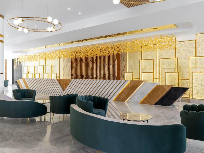 Moderne hotel lobby met gebogen fluwelen banken, gouden accenten en een decoratieve wand achter de receptie.