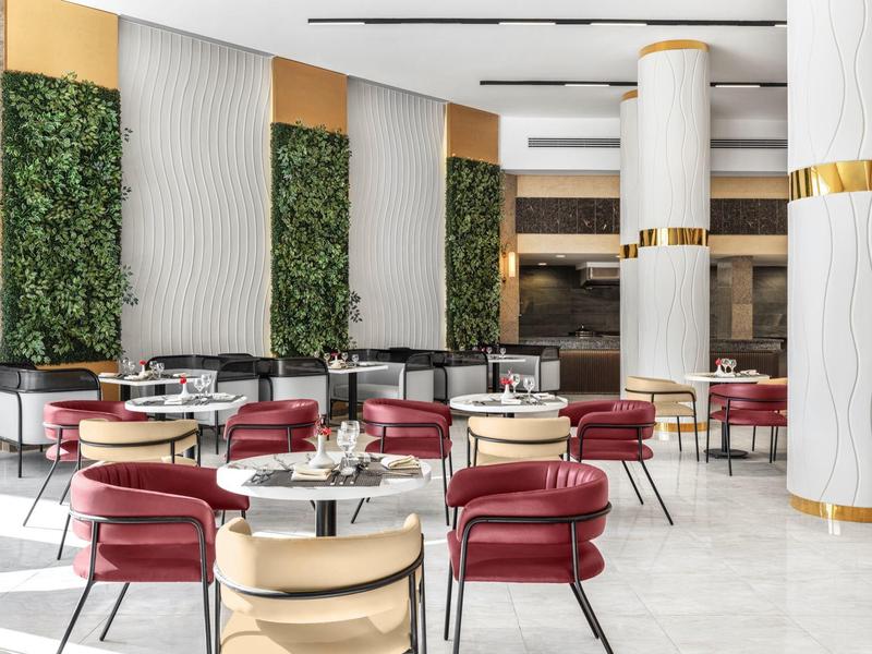 Moderne hotelrestaurant met elegante tafels, rode en crème stoelen en groene wandpanelen.