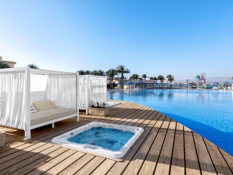 Luxe cabana's bij het zwembad aan een infinity pool onder een heldere blauwe lucht.