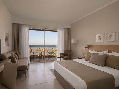 Chambre d'hôtel lumineuse avec lit double, coin salon et vue sur la mer par de grandes fenêtres.