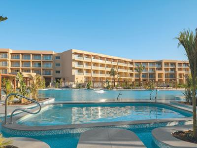 Grande hotel su più piani con piscina all'aperto sotto un cielo sereno.