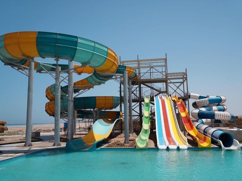Plusieurs toboggans colorés mènent à une grande piscine sous un ciel clair.