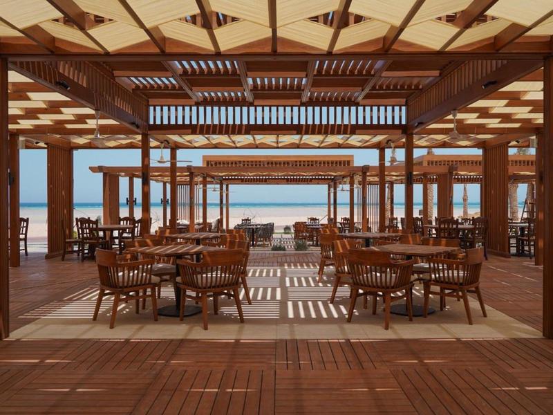 Restaurant de plage ouvert avec mobilier en bois et vue sur la mer sous un toit en bois structuré.