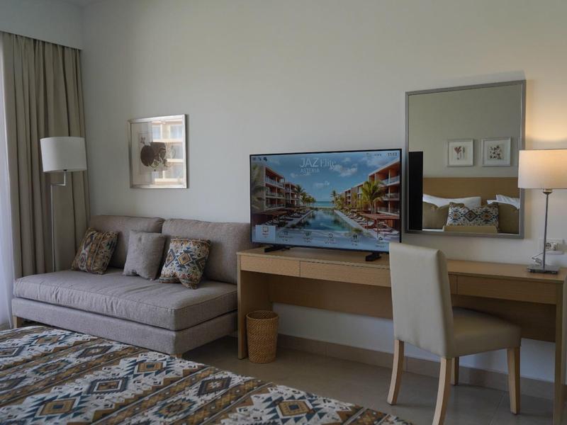 Chambre d'hôtel moderne avec canapé, bureau, chaise et grand téléviseur à écran plat.