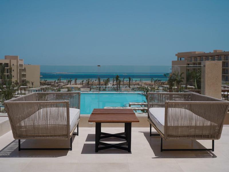 Deux chaises et une table près de la piscine avec vue sur la mer et ciel bleu clair.