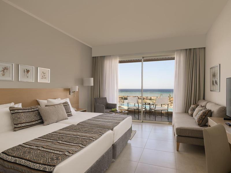 Chambre d'hôtel lumineuse avec deux lits, vue sur la mer et balcon avec coin salon