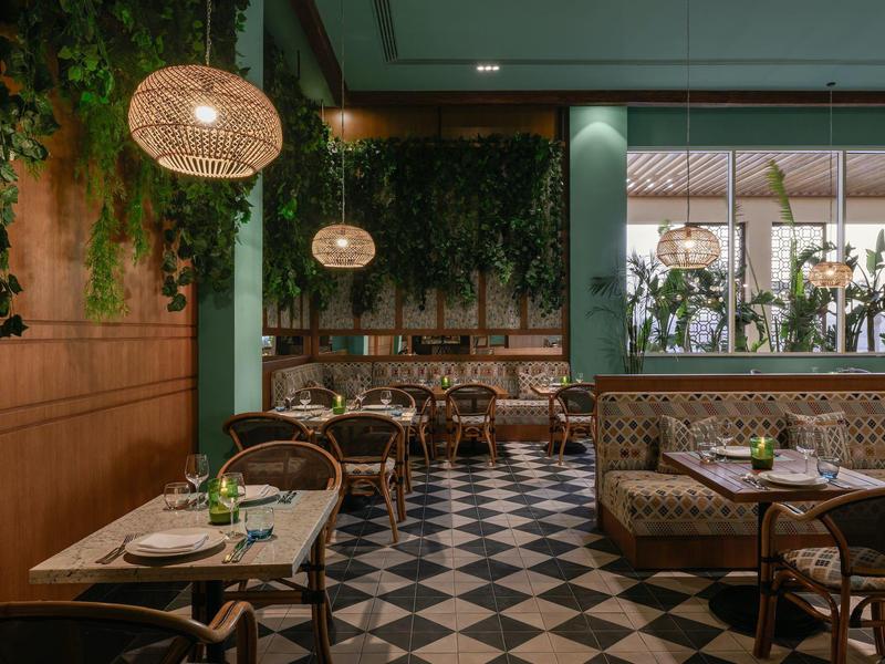 Intérieur de restaurant cosy avec plantes vertes, sol en bois et carrelage, tables et chaises élégantes.