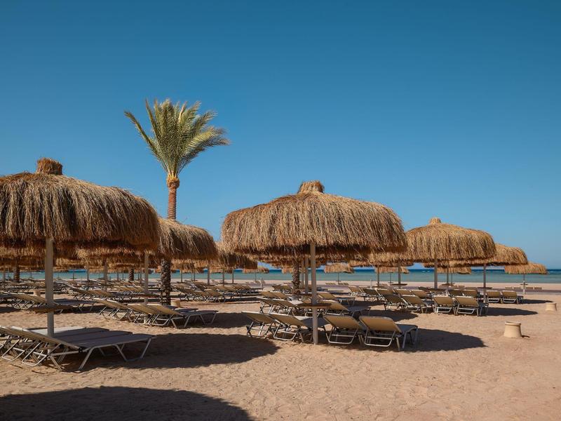 Plage avec parasols en feuilles de palmier et chaises longues sous un ciel clair.