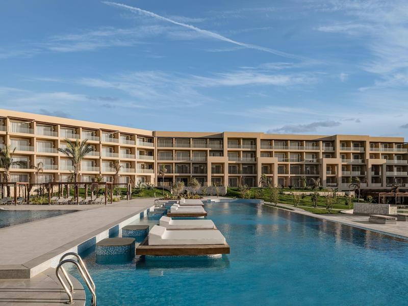 Complexe hôtelier moderne avec grande piscine, transats dans l'eau et palmier sous ciel clair