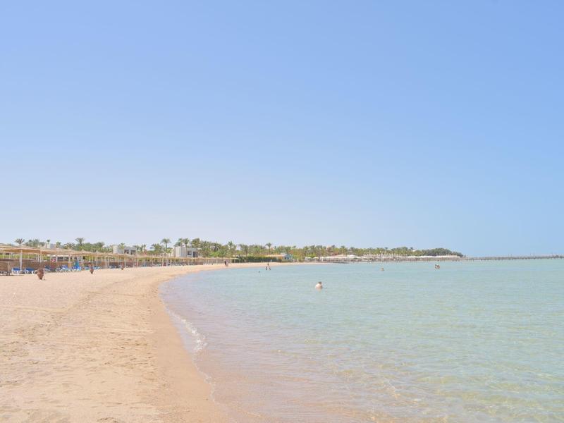 Weicher Sandstrand mit klarem, ruhigem Wasser unter hellem, wolkenlosem Himmel.