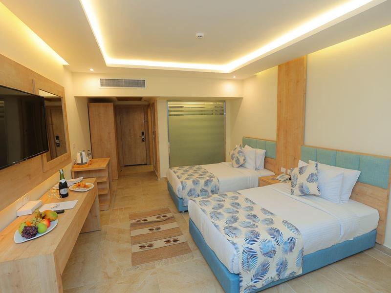 Modernes Hotelzimmer mit zwei Einzelbetten, Holzmöbeln, Flachbildschirm und indirekter Beleuchtung.