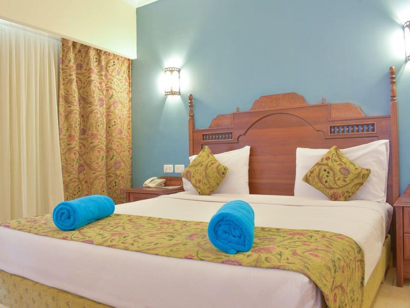 Gemütliches Hotelzimmer mit großem Bett, bunten Kissen, blauen Handtüchern und sanfter Beleuchtung.