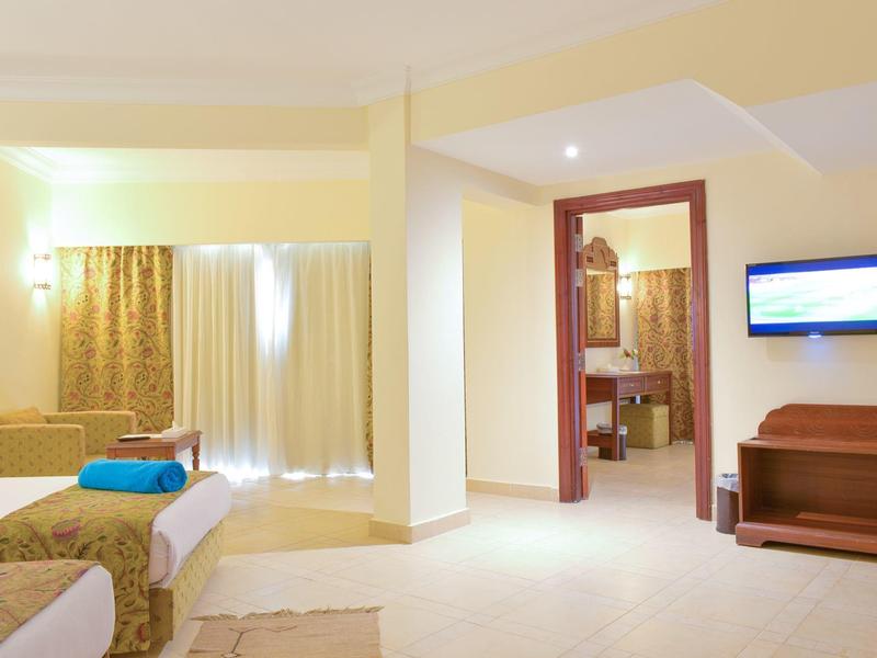 Hell eingerichtetes Hotelzimmer mit Doppelbett, Vorhängen, Bad und Fernseher an der Wand.