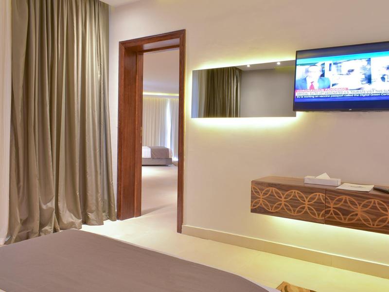 Modernes Hotelzimmer mit offenem Vorhang, Wandfernseher und Holzdekor unter Spiegelleuchte.