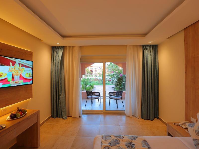 Helles modernes Schlafzimmer mit Holzboden, TV an der Wand und Terrassentür zu Balkon mit Gartenblick.