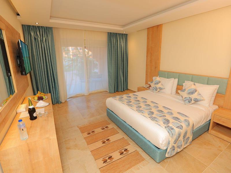 Helles Schlafzimmer mit Doppelbett, Holzmöbeln, blauen Vorhängen und zwei Teppichen auf Fliesenboden.