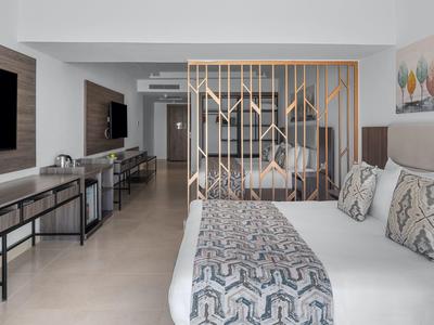 Modernes Hotelzimmer mit Doppelbett, Holzwandtrenner und Sitzbereich, in hellen Farben gestaltet.