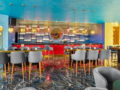 Moderne Bar mit blauem Decke, grauen Stühlen, rotem Tresen und schwarzem Marmorboden.