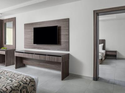 Moderner Raum mit Flachbildschirm, Holzmöbeln und Blick in angrenzendes Schlafzimmer.