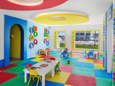 Bunter Kinderspielraum mit bunten Stühlen, Tischen, Teppichfliesen und Wanddekoration.