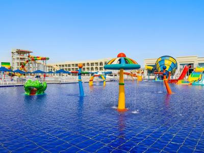 Wasserspielplatz mit bunten Rutschen, Sprinklern und flachem Wasser unter blauem Himmel.
