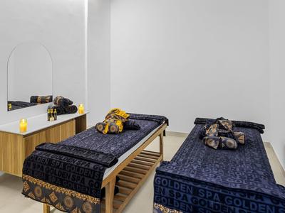 Zwei Massageliegen mit dunklen Tüchern in hellem, minimalistisch gestaltetem Raum mit Holzkonsole und Spiegel.