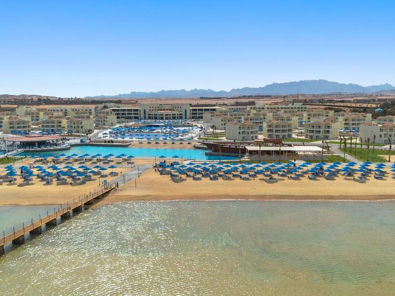 Großes Resort mit Strand, vielen Liegestühlen und Pools vor klarer Meeresküste.