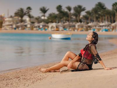 Woman relaxing on sandy beach near calm water and palm trees