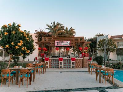 Offene Bar mit roten Hockern und Holztischen neben einem Pool in einer Hotelanlage.