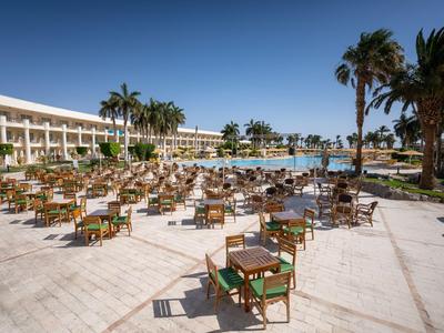 Außenbereich eines Hotels mit vielen Tischen und Stühlen, Palmen und blauem Himmel.