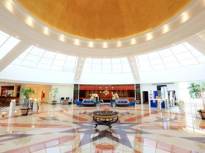Bright hotel lobby with large circular ceiling, marble floor, and seating areas.
