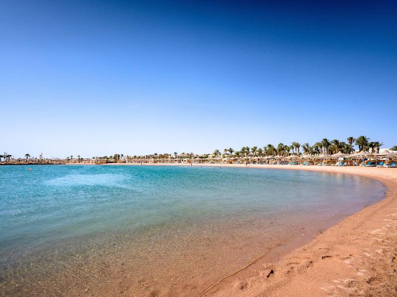 Wide sandy beach with calm clear water and blue sky at a sunny vacation spot.