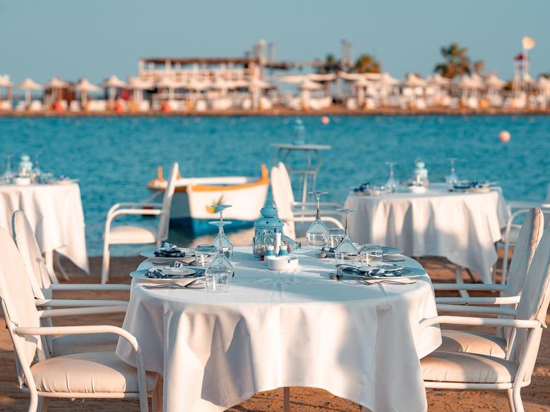 Restaurant table with white cloth by the water, overlooking the sea and distant buildings.