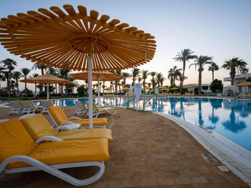 Hotel pool with yellow loungers and large umbrellas at sunset.