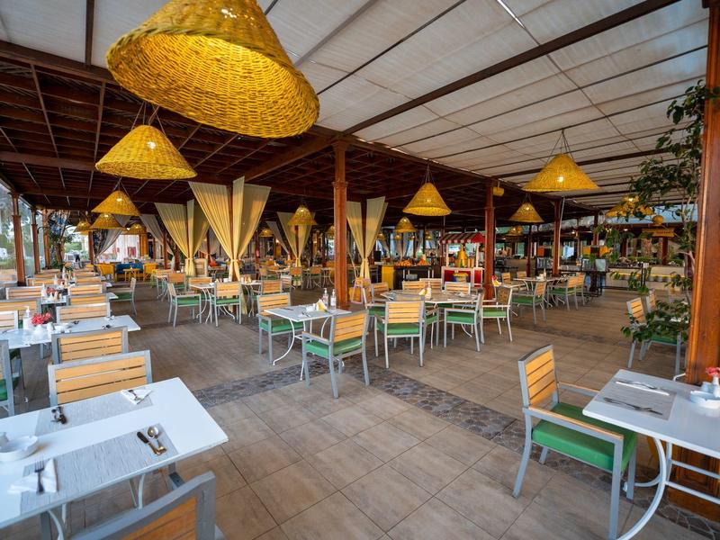 Bright restaurant with wooden floor, many tables and chairs, and yellow lampshades.