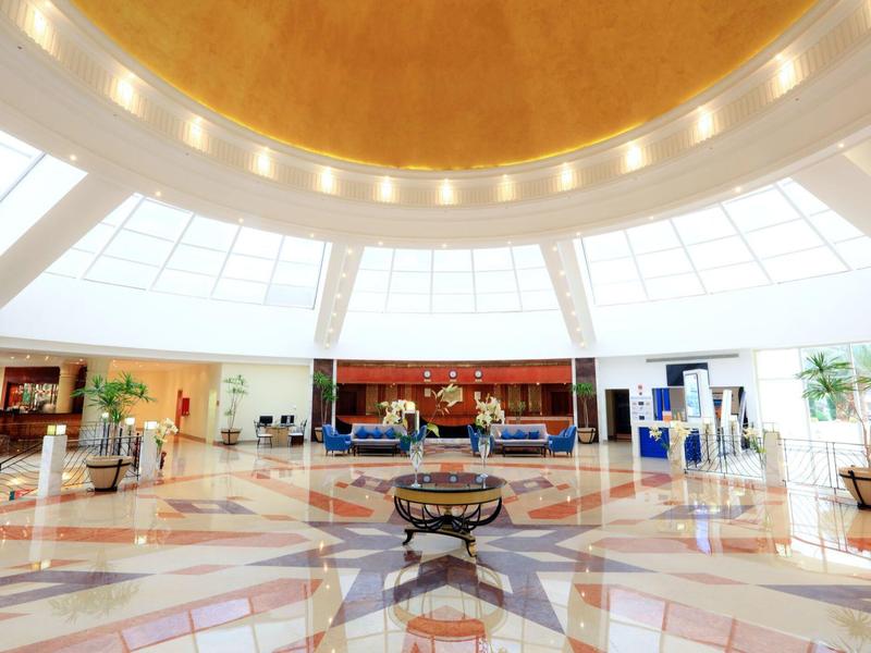 Bright hotel lobby with large circular ceiling, marble floor, and seating areas.